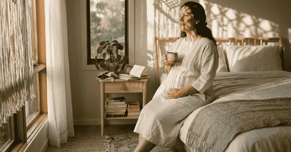 Mulher grávida depois dos 40 anos com mãos na barriga em luz natural quente